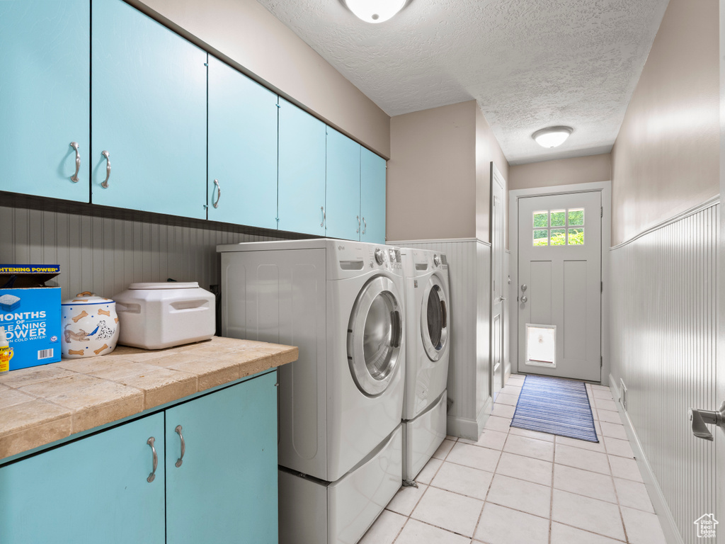 Laundry room featuring cabinet space, washing machine and dryer, a textured ceiling, light tile patterned floors, and a wainscoted wall