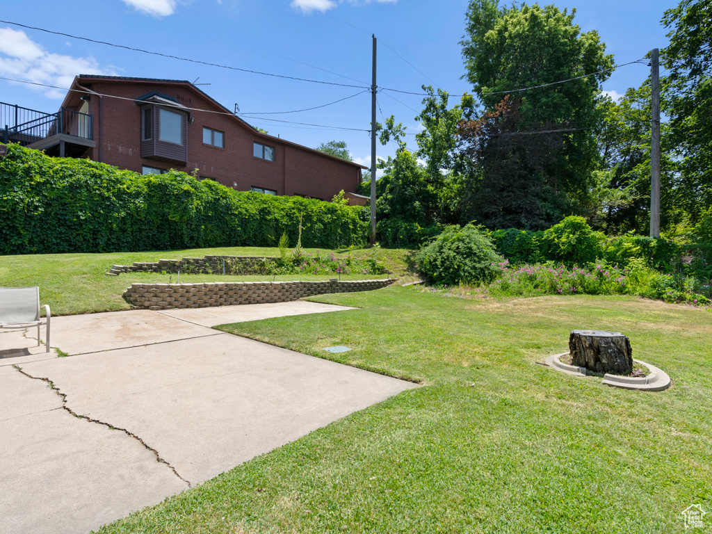 View of grassy yard featuring an outdoor fire pit and a patio area