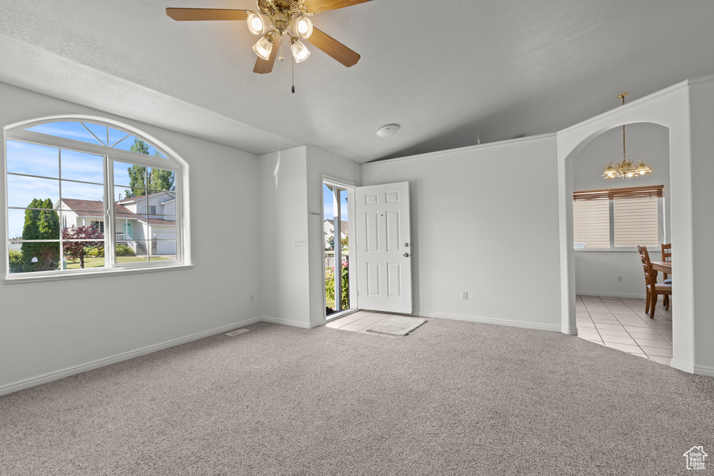 Carpeted empty room featuring a chandelier, healthy amount of natural light, ceiling fan, lofted ceiling, and arched walkways