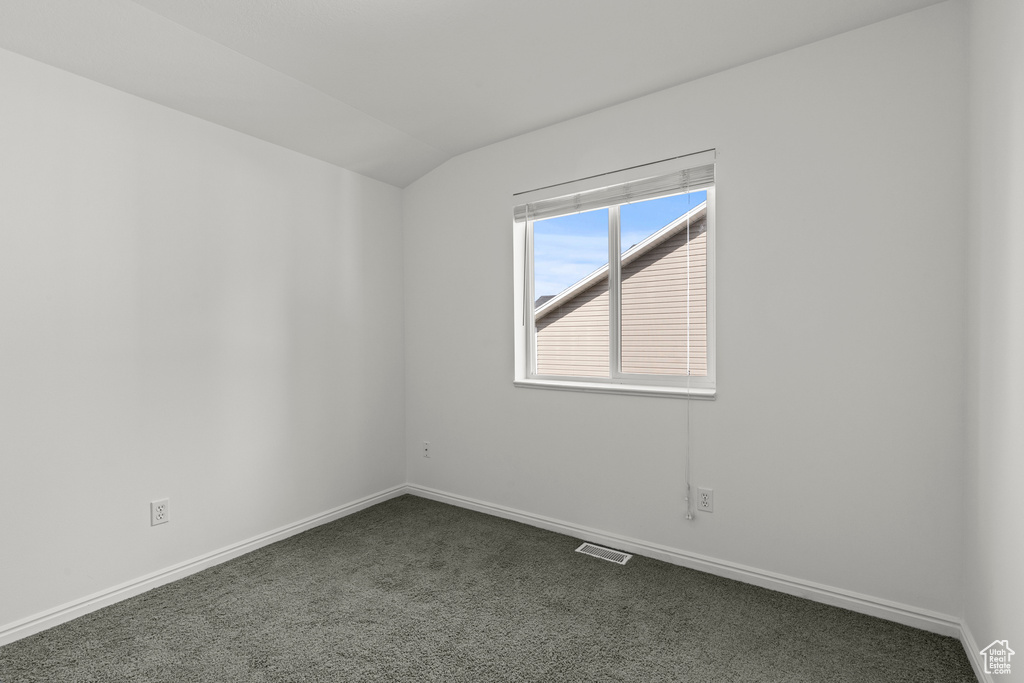 Unfurnished room featuring dark colored carpet and lofted ceiling