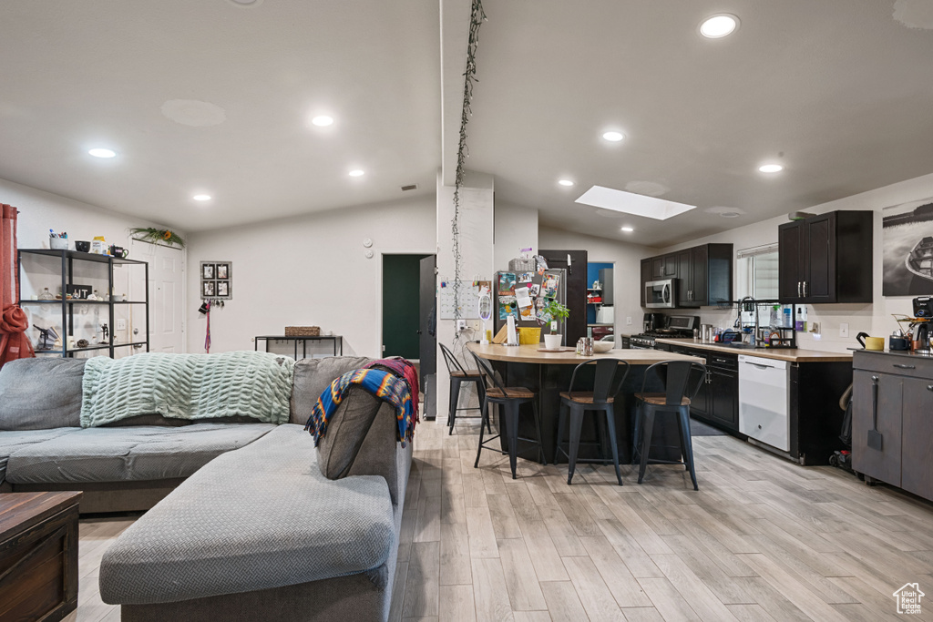Living area with a skylight, light wood-style flooring, vaulted ceiling, and recessed lighting