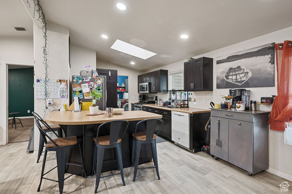 Kitchen with appliances with stainless steel finishes, a skylight, a breakfast bar, light wood-style floors, and vaulted ceiling
