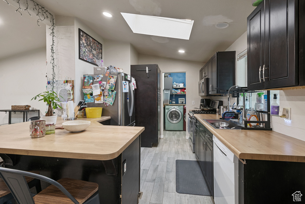 Kitchen featuring washer / dryer, stainless steel appliances, butcher block counters, a skylight, and dark cabinets