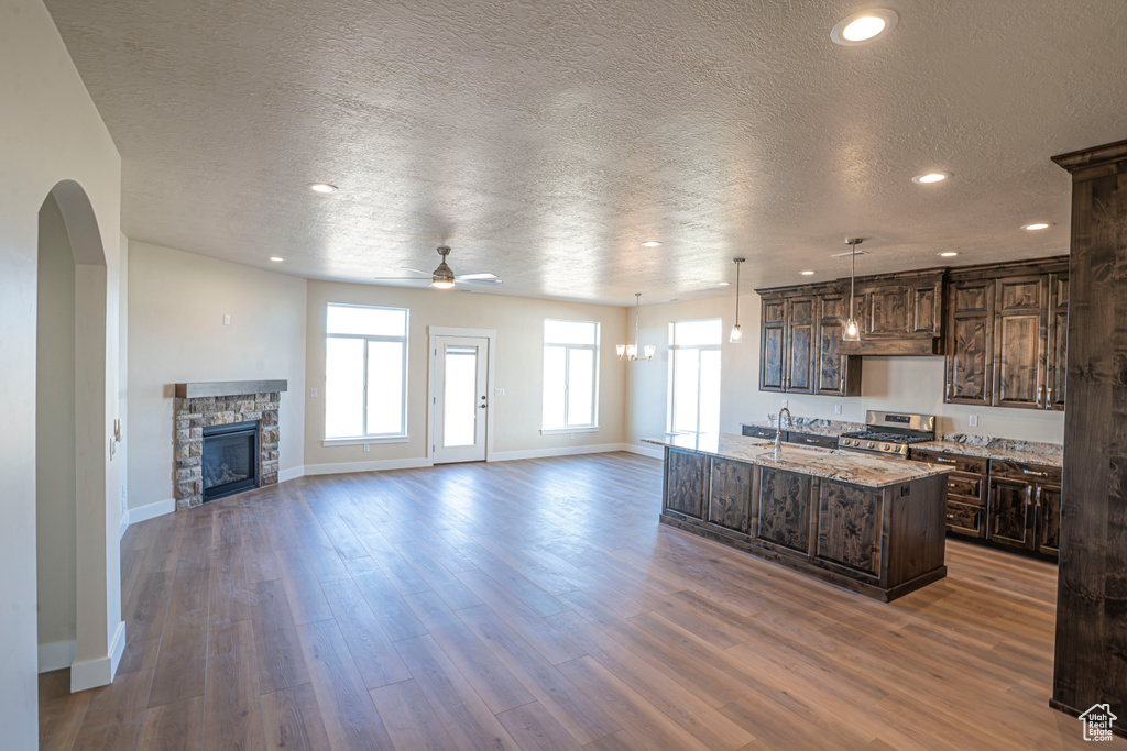 Kitchen with ceiling fan, stainless steel gas stove, a textured ceiling, dark brown cabinetry, and a stone fireplace