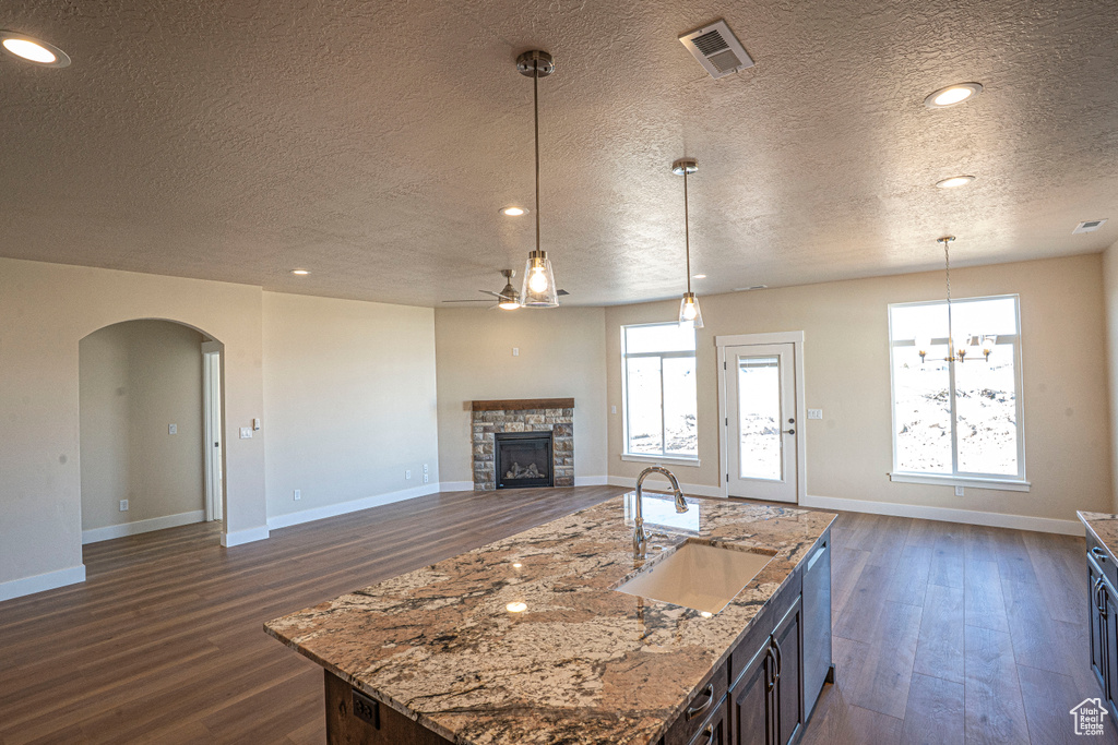 Kitchen featuring a textured ceiling, arched walkways, ceiling fan, open floor plan, and a stone fireplace