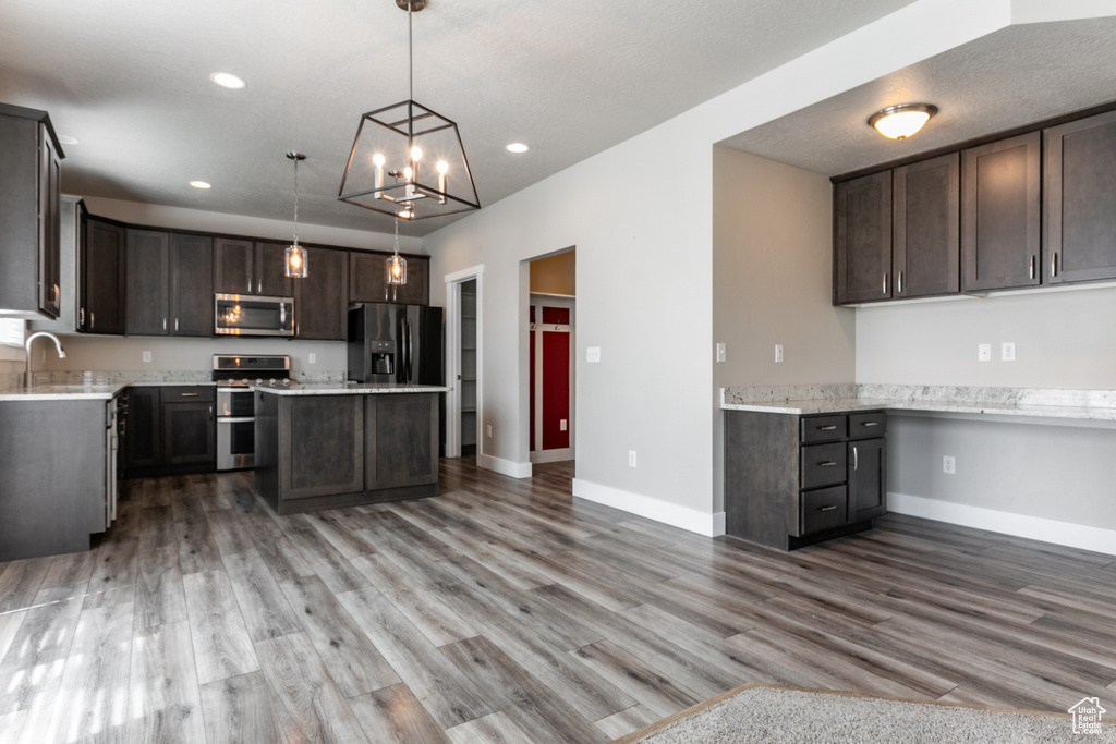 Kitchen with stainless steel appliances, dark brown cabinetry, light countertops, wood finished floors, and a center island