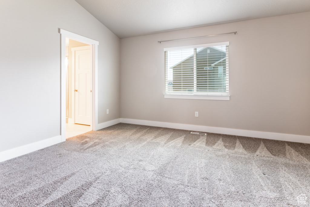 Carpeted spare room featuring lofted ceiling and baseboards
