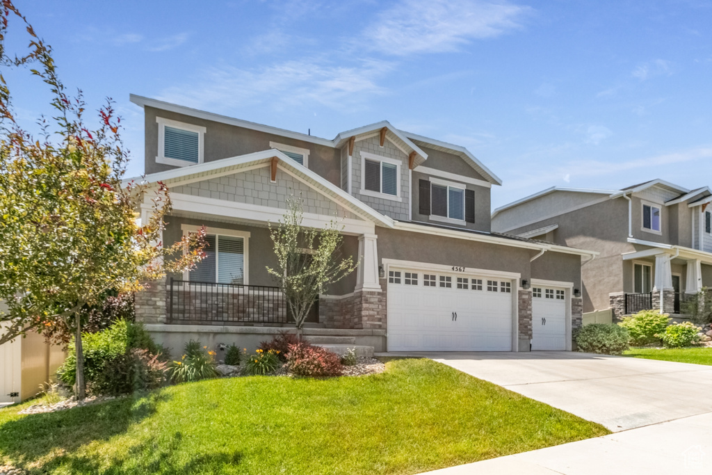 View of front of property featuring stucco siding, a front yard, stone siding, driveway, and covered porch