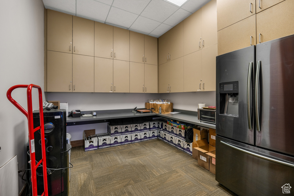 Kitchen featuring stainless steel refrigerator with ice dispenser, cream cabinets, carpet, and a drop ceiling