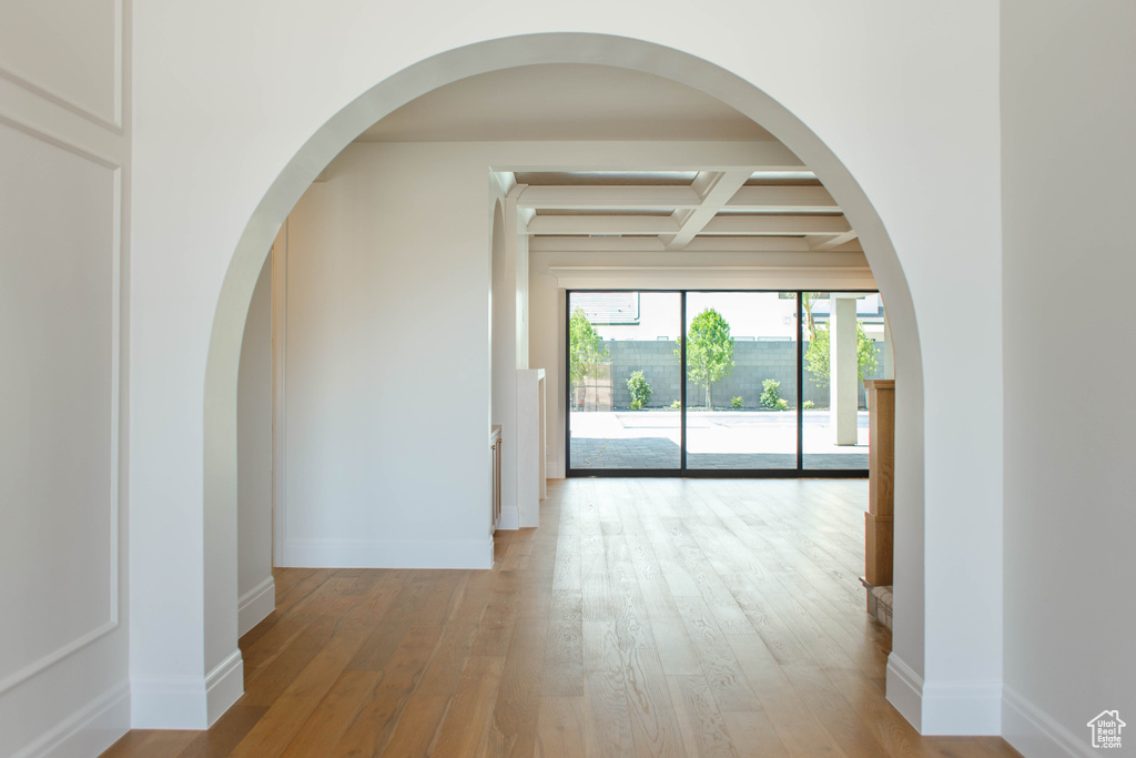 Empty room featuring coffered ceiling, beam ceiling, wood finished floors, and arched walkways