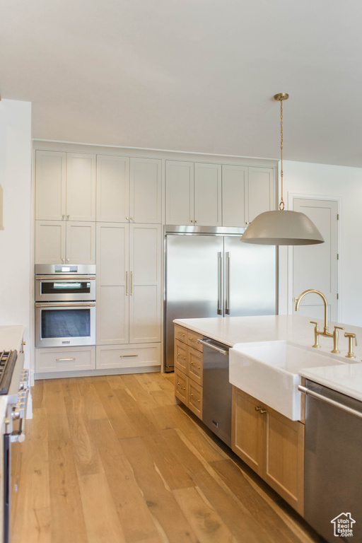 Kitchen featuring appliances with stainless steel finishes, light wood-type flooring, light countertops, and pendant lighting