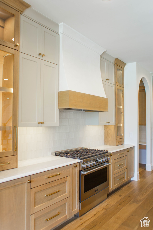 Kitchen featuring high end stainless steel range, arched walkways, premium range hood, light countertops, and light wood-type flooring