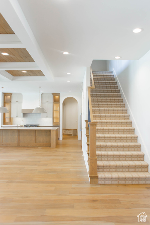 Staircase with wood finished floors, beamed ceiling, recessed lighting, and arched walkways
