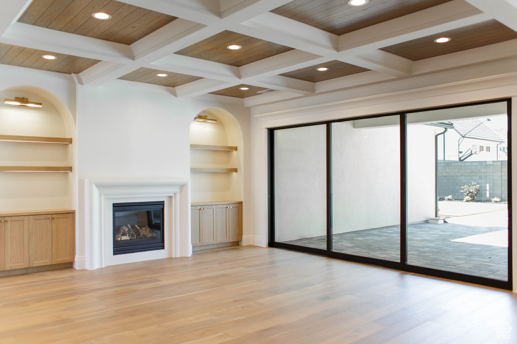 Unfurnished living room with a glass covered fireplace, light wood-type flooring, built in features, recessed lighting, and beamed ceiling