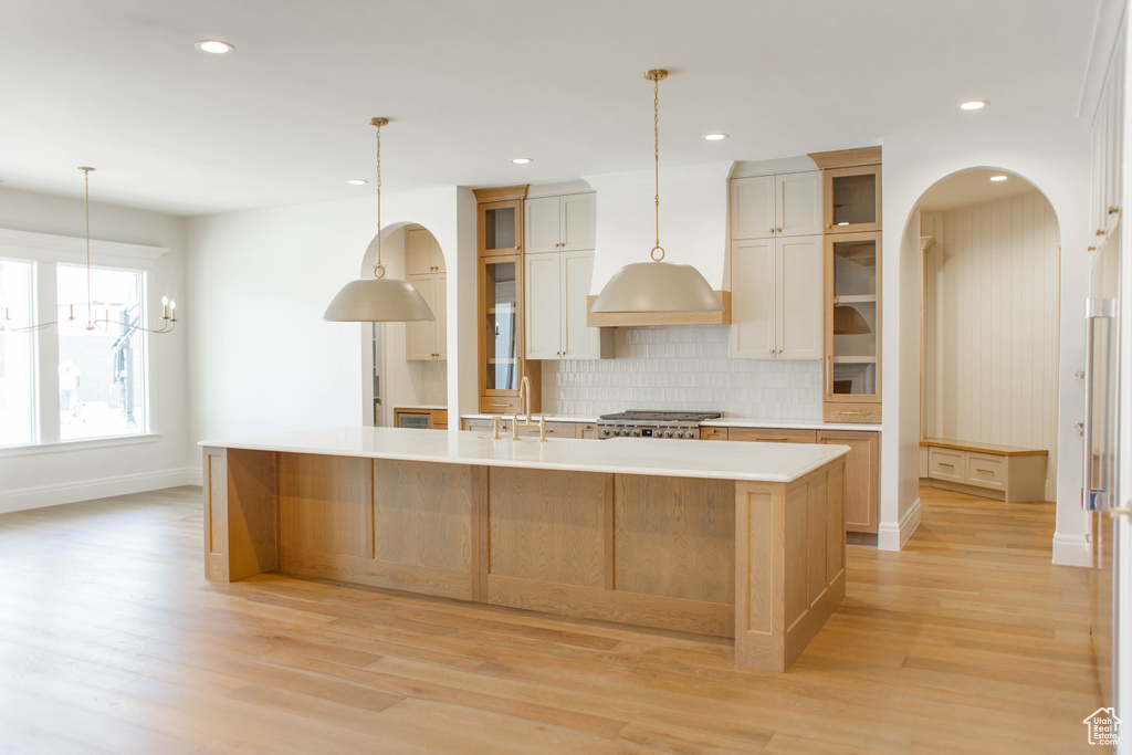 Kitchen with a large island with sink, tasteful backsplash, light wood-type flooring, light countertops, and recessed lighting