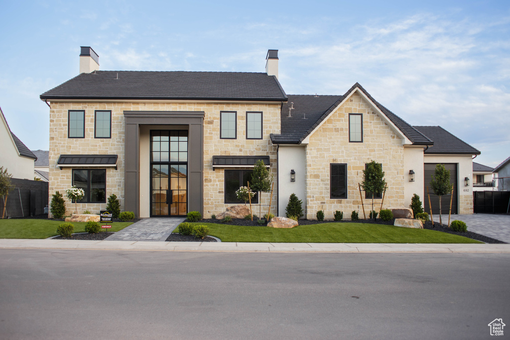 View of front facade featuring a chimney, stone siding, and a front lawn