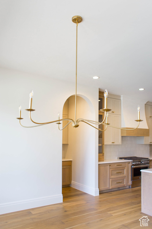 Kitchen with stainless steel range, light wood-style floors, backsplash, recessed lighting, and a chandelier
