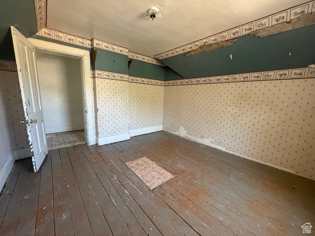 Spare room with dark wood-style floors, wallpapered walls, and lofted ceiling