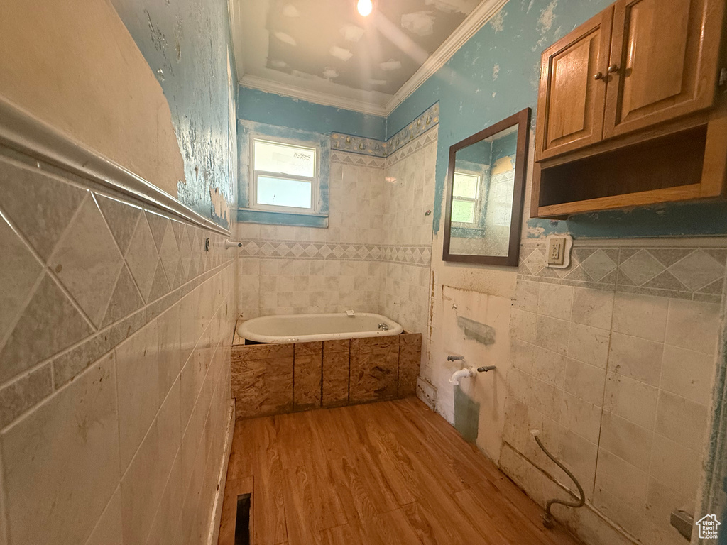 Full bath with tile walls, a bath, wood finished floors, and ornamental molding