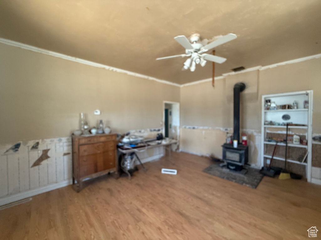 Living area with ceiling fan, wood finished floors, crown molding, and a wood stove