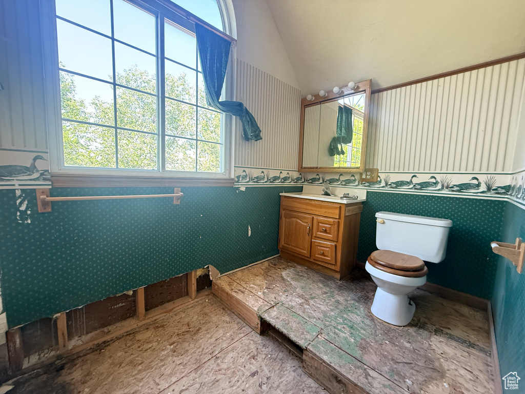Bathroom with plenty of natural light, vanity, wallpapered walls, wainscoting, and vaulted ceiling