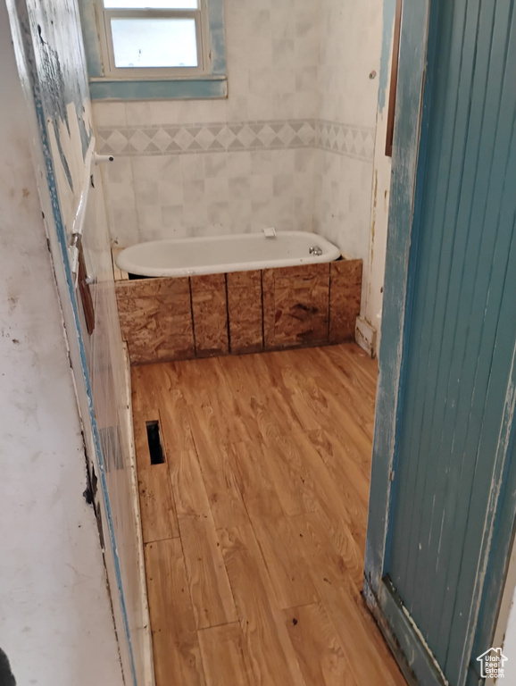 Full bathroom featuring a garden tub, wood finished floors, tile walls, and wainscoting