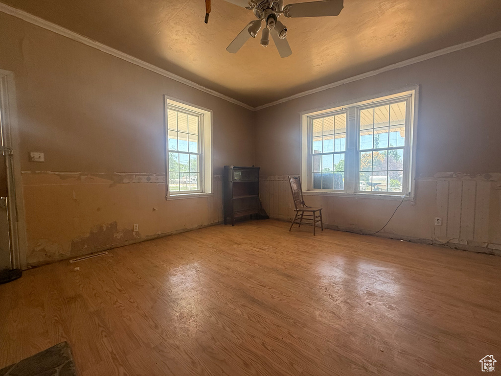 Empty room featuring wood finished floors, crown molding, ceiling fan, and radiator heating unit