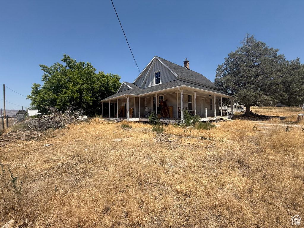 View of front of property featuring a porch, a chimney, and roof with shingles