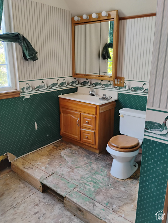 Bathroom featuring wallpapered walls, vanity, and vaulted ceiling