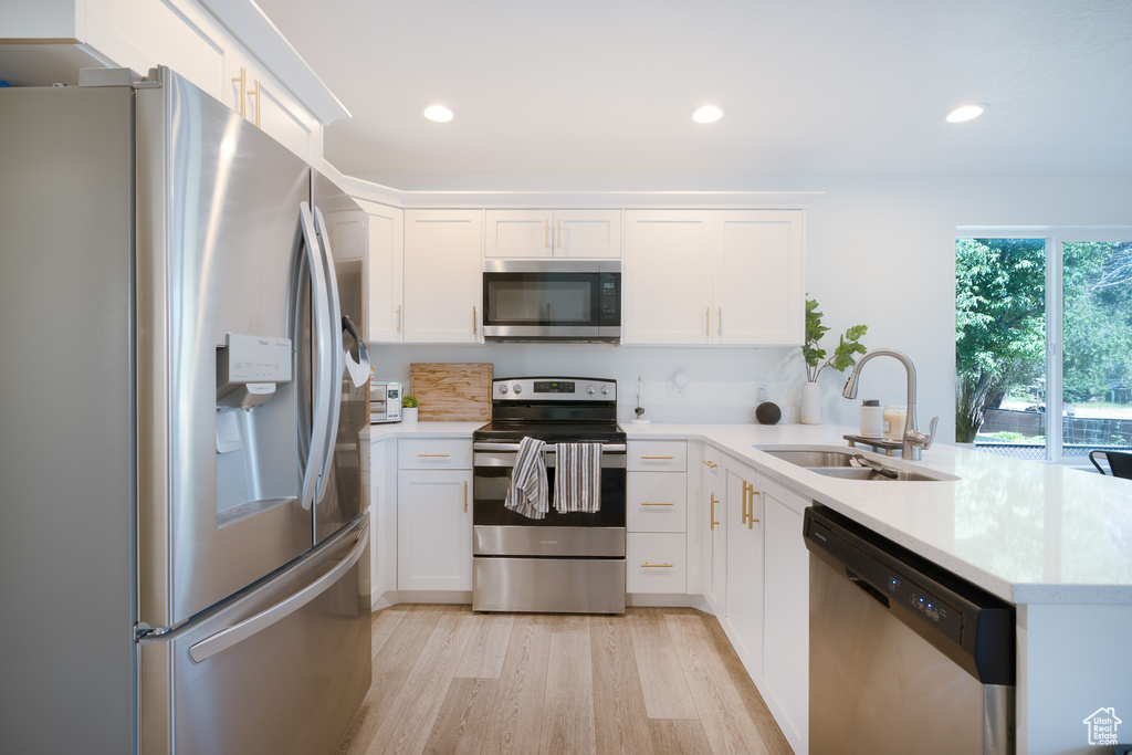 Kitchen featuring appliances with stainless steel finishes, a peninsula, light wood finished floors, white cabinets, and recessed lighting