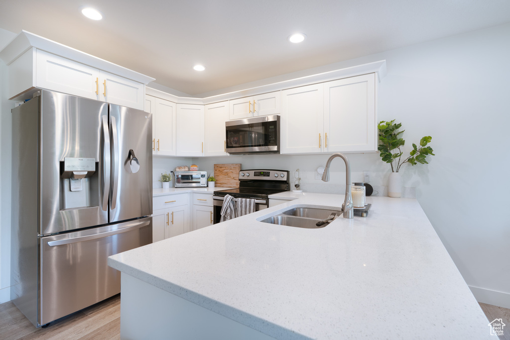 Kitchen featuring appliances with stainless steel finishes, a peninsula, light wood-type flooring, white cabinetry, and recessed lighting