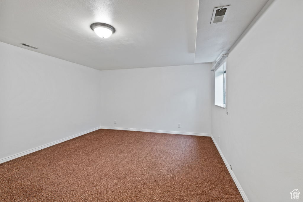 Spare room featuring dark colored carpet and baseboards