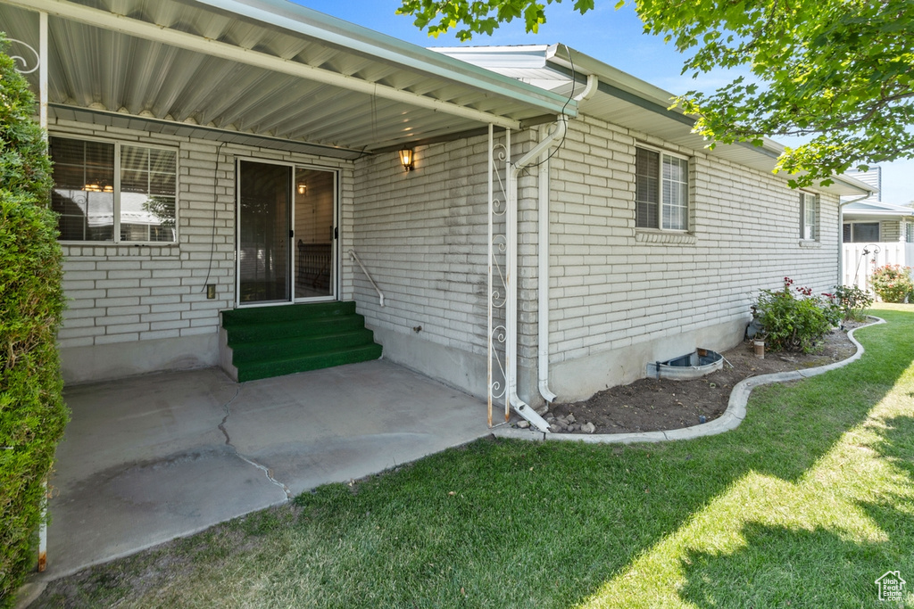Rear view of house featuring entry steps, a lawn, and a patio