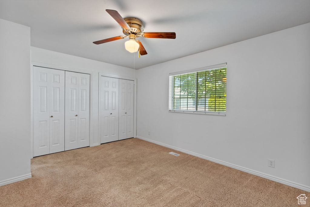 Unfurnished bedroom with carpet floors, two closets, and a ceiling fan