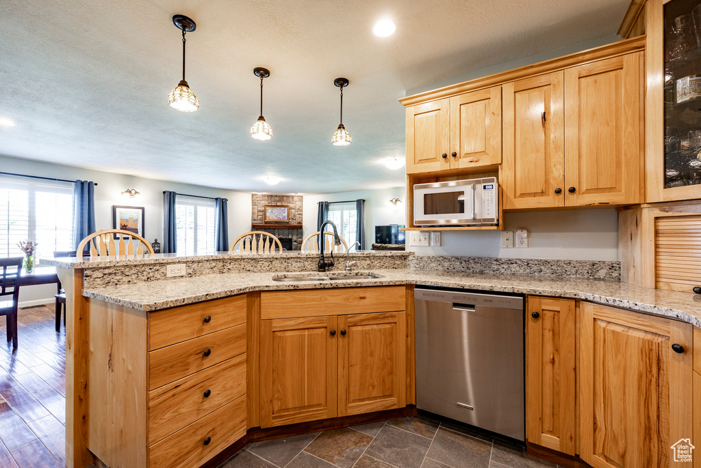 Kitchen featuring stainless steel dishwasher, white microwave, a peninsula, light stone countertops, and hanging light fixtures