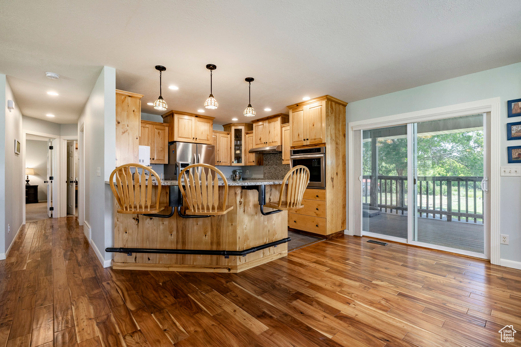 Kitchen featuring stainless steel appliances, dark wood-style floors, light brown cabinetry, a breakfast bar, and recessed lighting