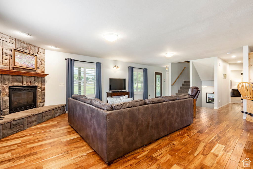Living area with a stone fireplace, stairs, and light wood-style floors
