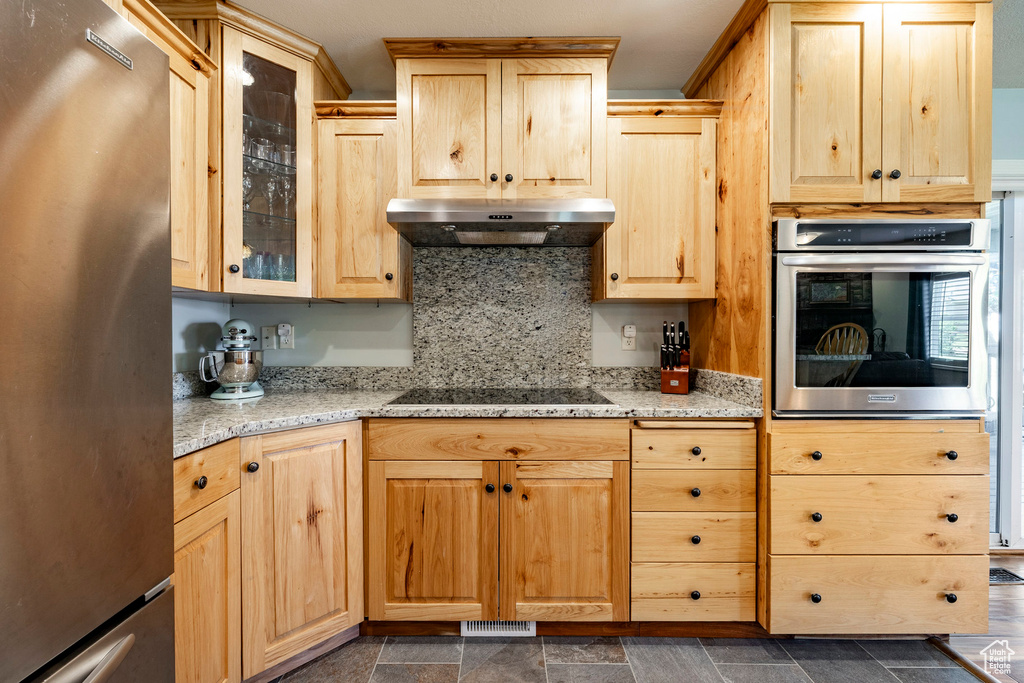 Kitchen with stainless steel appliances, under cabinet range hood, light brown cabinetry, and glass insert cabinets