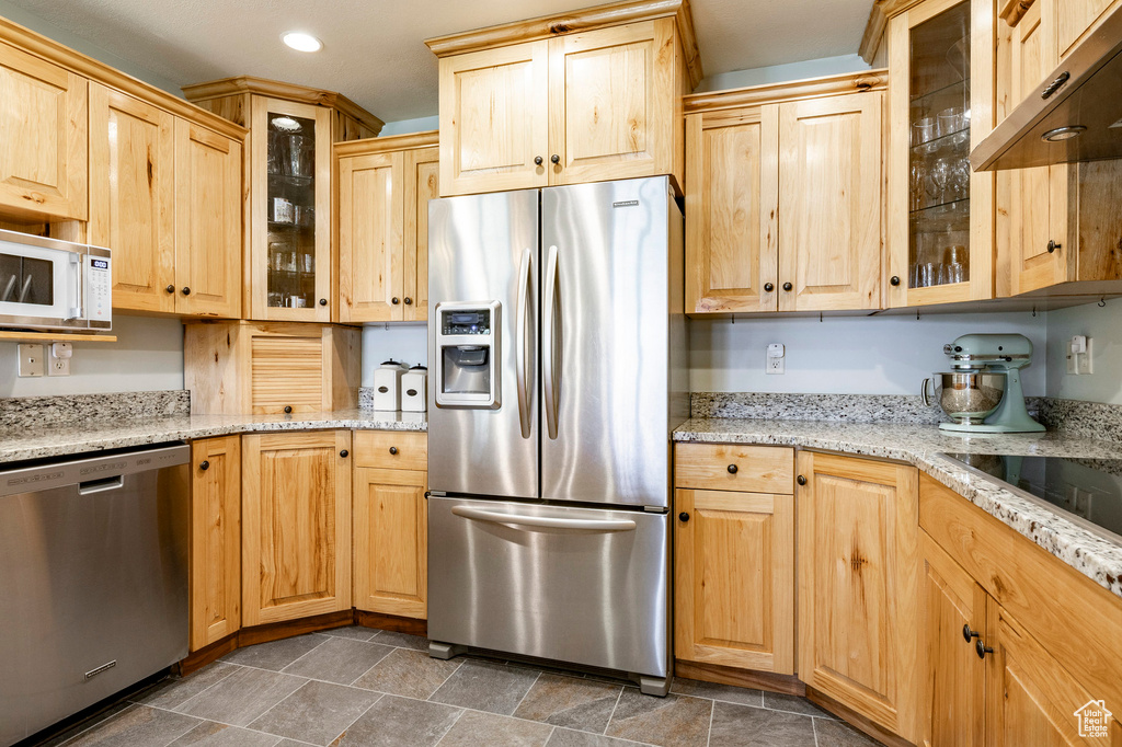 Kitchen with stainless steel appliances, extractor fan, recessed lighting, light brown cabinetry, and light stone counters
