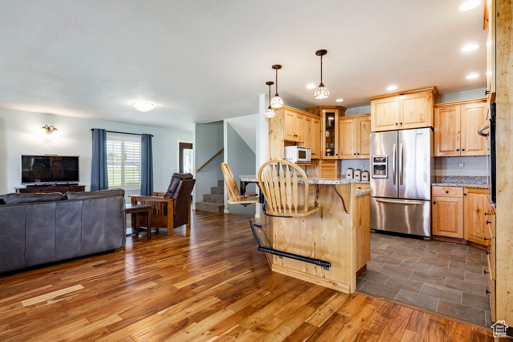 Kitchen with stainless steel refrigerator with ice dispenser, open floor plan, light brown cabinets, glass insert cabinets, and a breakfast bar