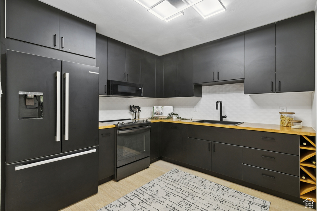 Kitchen with black appliances, light wood-style floors, dark cabinetry, and decorative backsplash
