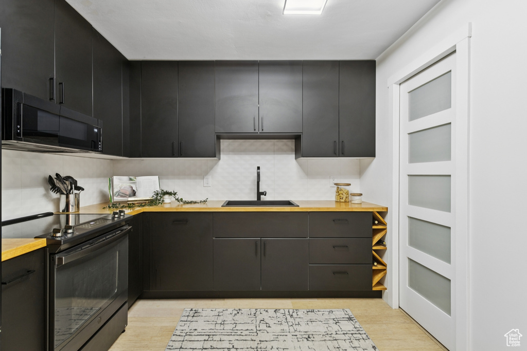 Kitchen featuring black appliances, butcher block counters, light wood-style flooring, dark cabinetry, and backsplash