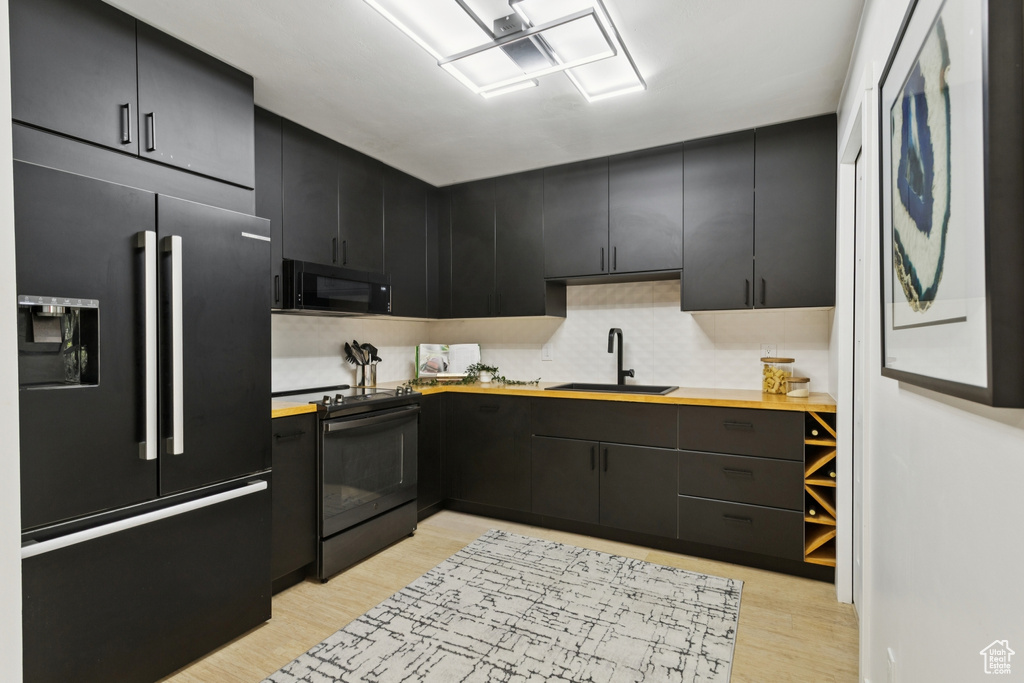 Kitchen with black appliances, dark cabinets, light wood finished floors, butcher block countertops, and tasteful backsplash