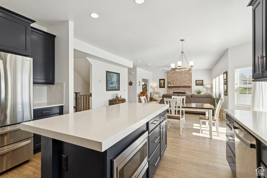 Kitchen with appliances with stainless steel finishes, light countertops, light wood-style flooring, a center island, and open floor plan