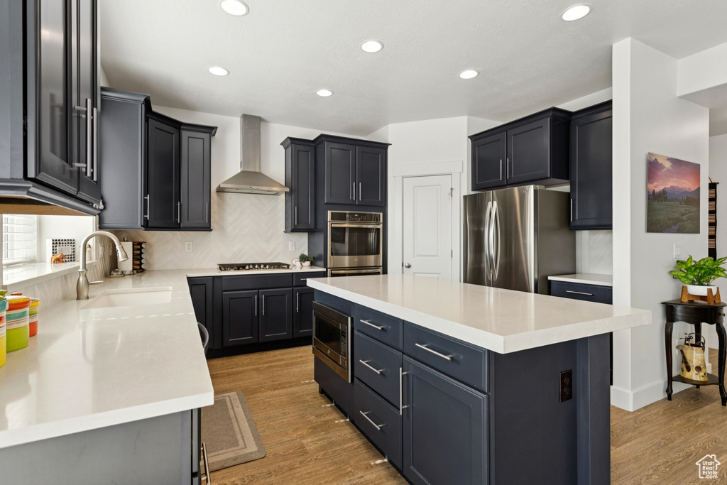 Kitchen featuring appliances with stainless steel finishes, wall chimney range hood, backsplash, a center island, and recessed lighting