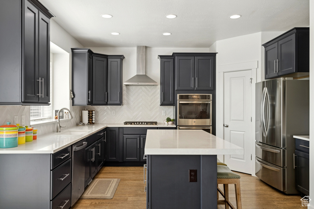 Kitchen featuring stainless steel appliances, wall chimney exhaust hood, a kitchen island, tasteful backsplash, and a breakfast bar area