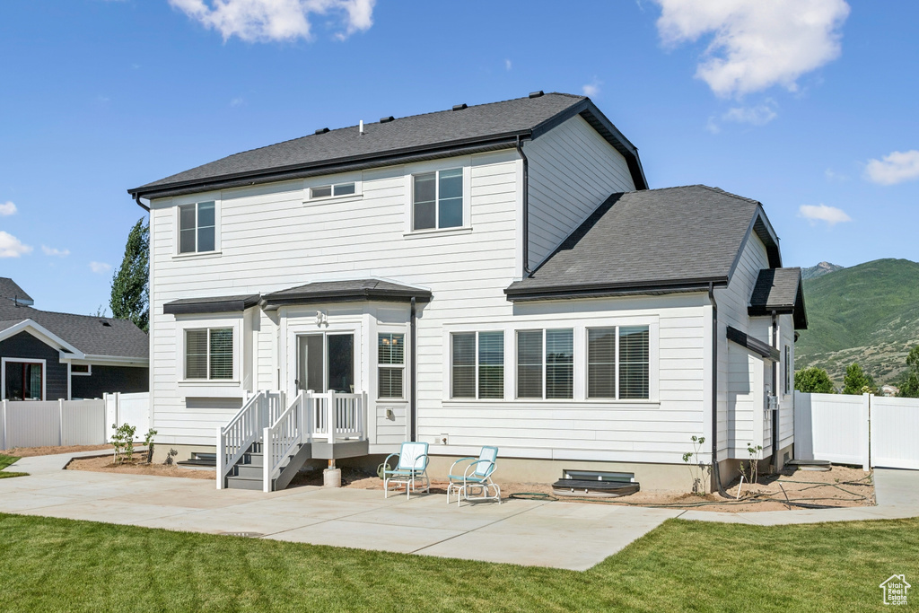 Rear view of house featuring a patio area, a mountain view, and a shingled roof