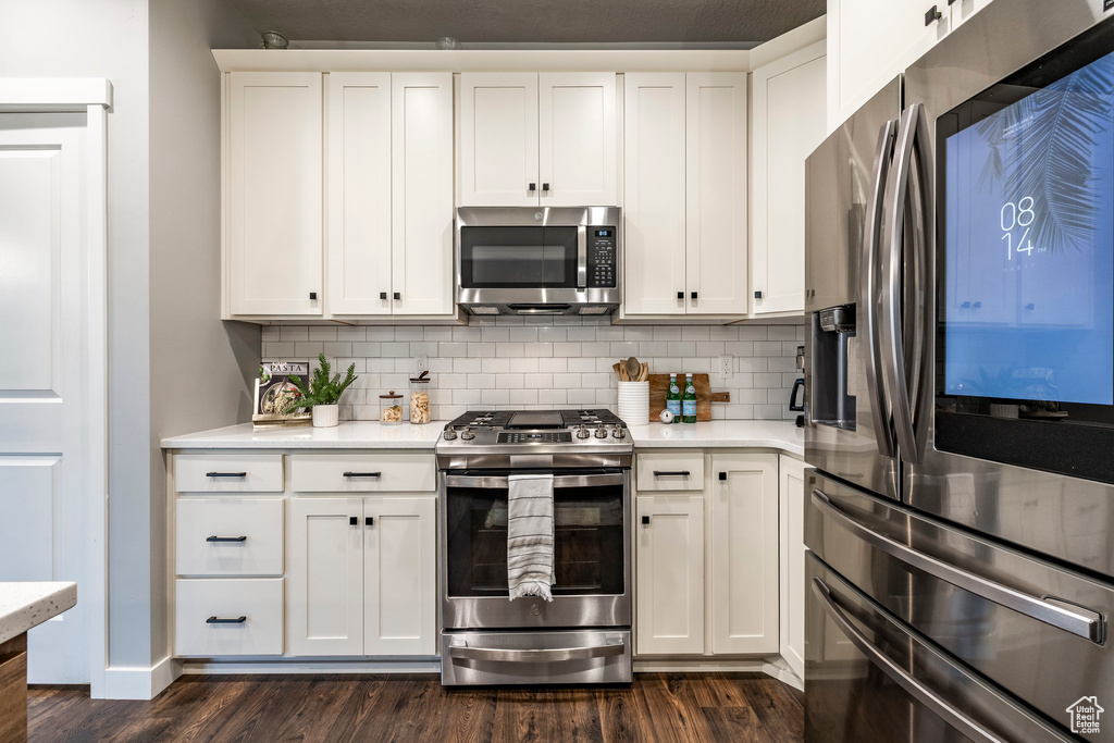 Kitchen with stainless steel appliances, dark wood-style floors, light countertops, tasteful backsplash, and white cabinets