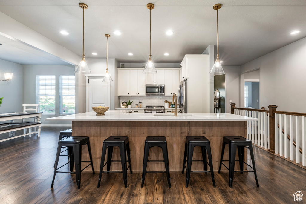 Kitchen with appliances with stainless steel finishes, dark wood-style floors, light countertops, a large island with sink, and white cabinetry