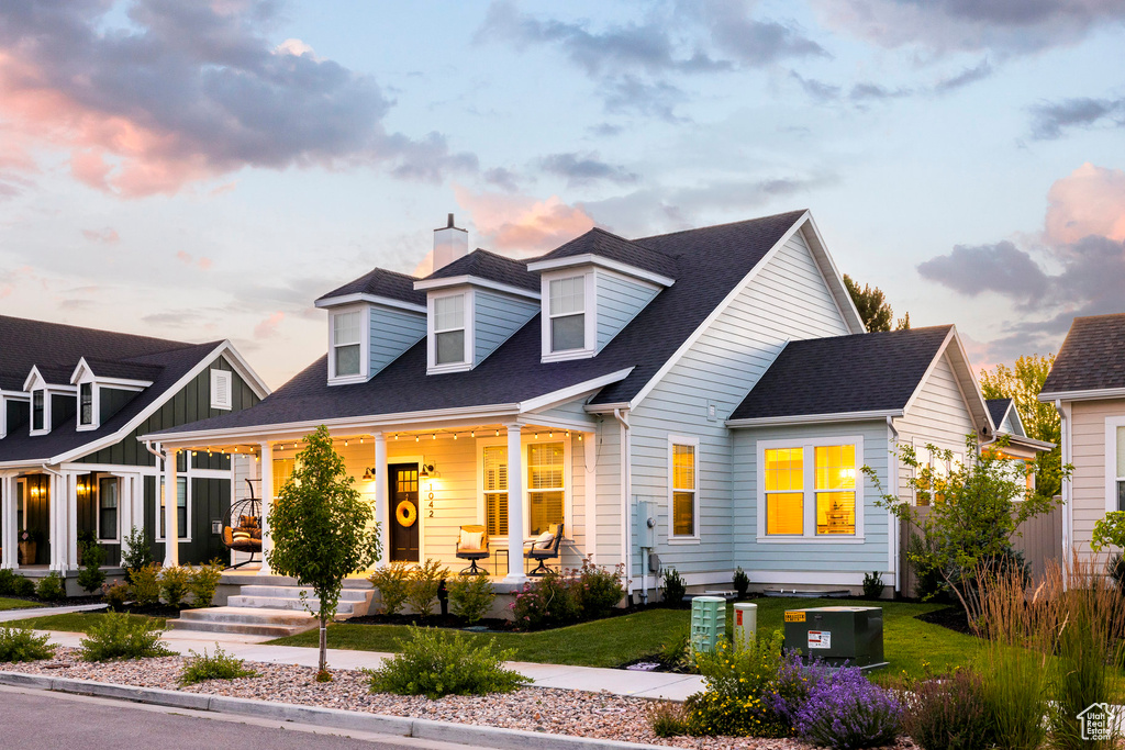 Cape cod house featuring covered porch, a chimney, a shingled roof, and a yard